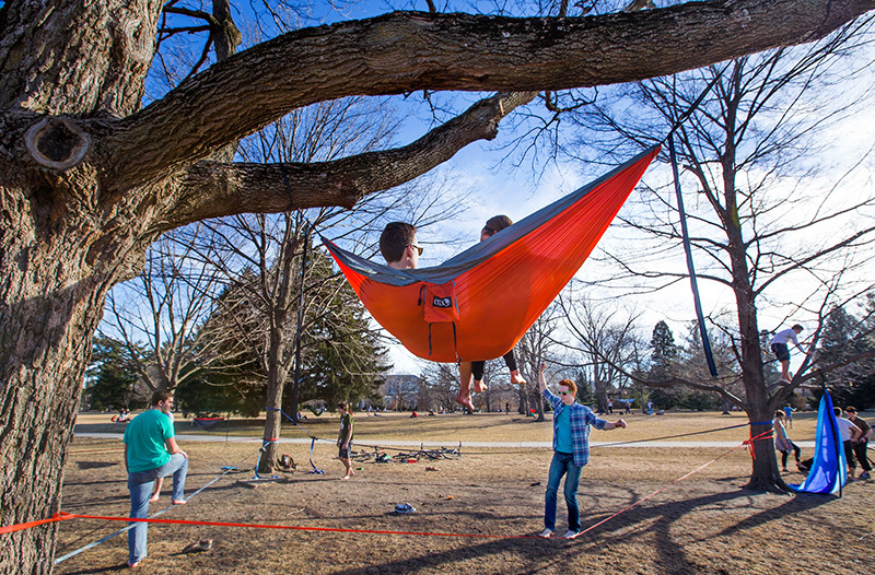 Two students walk a slack line while two observe from a hammock