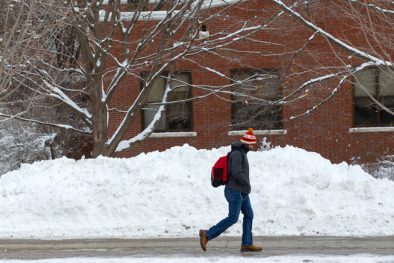 Male student passes snow pile adjacent to sidewalk