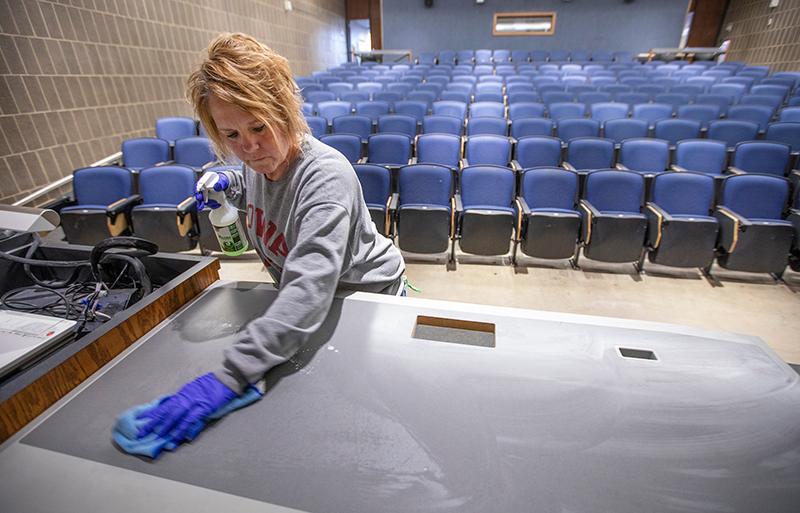 custodian disinfects a teaching table in an auditorium