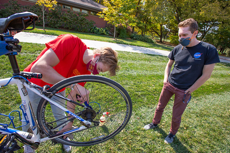 Male student tunes up another student's bike near Jischke Hall