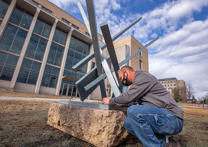 Worker secures metal sculpture to limestone base