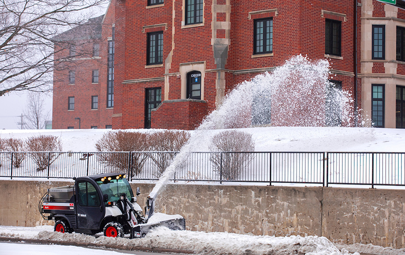 Campus services plow widens the path on a sidewalk south of Fril