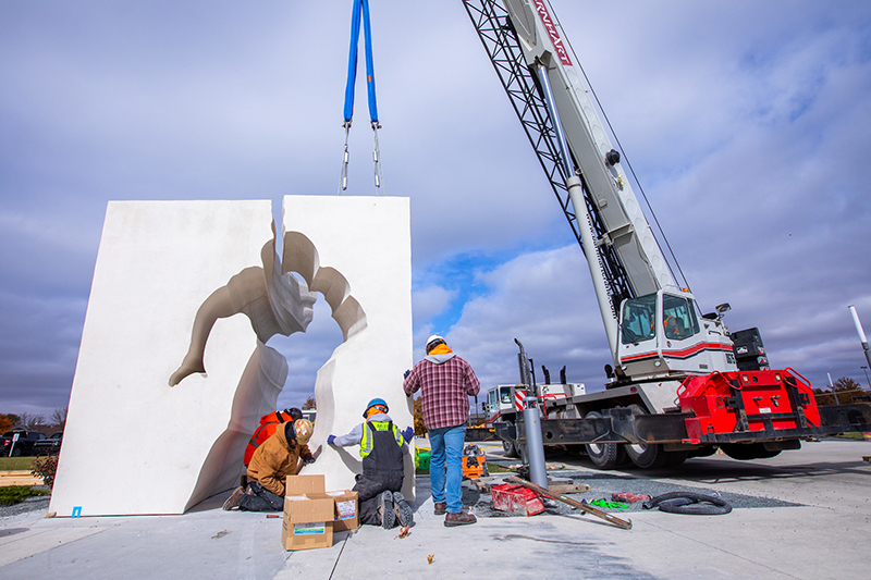 Crew lowers piece of sculpture into place via crane