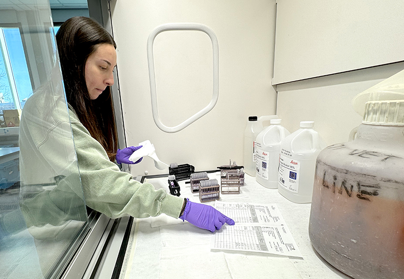 Woman in purple lab gloves checks slide samples against paper li