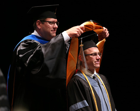 Professor places academic hood on graduating student
