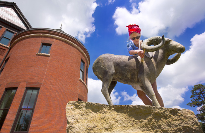 Woman in red kerchief applies wax to a big horn sheep sculpture