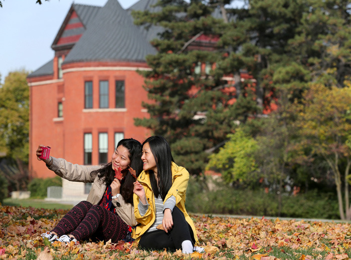 Two female students take a selfie in fallen leaves