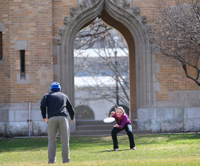 Male and female student play Frisbee near the campanile