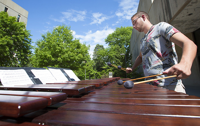 Male student plays the marimba outside in the sunshine