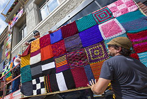 Workers raise knit squares on a wood frame