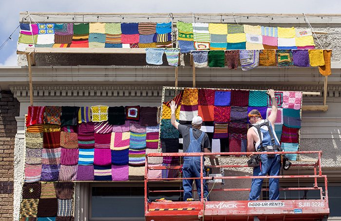 Workers raise a panel of knit squares into place on building front