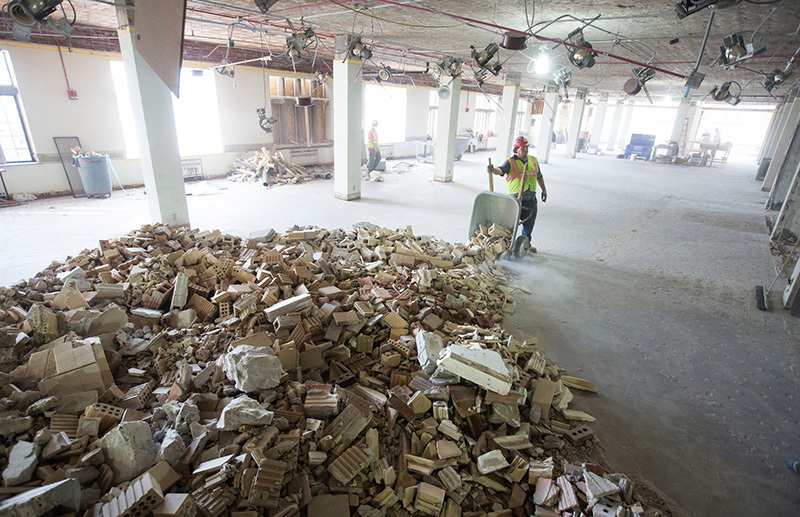 Man dumps wheel barrow of debris into pile inside