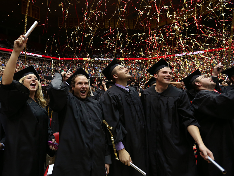 Four graudates in caps and gowns watch confetti fall