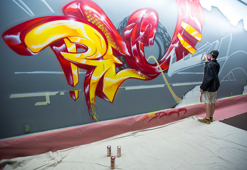 Alumnus Tim Westrom spray paints a wall mural in Beyer Hall