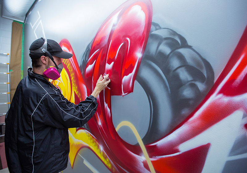 Alumnus Tim Westrom spray paints a wall mural