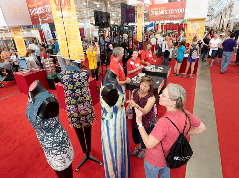 Women admire student-designed garments on mannequins at the fair