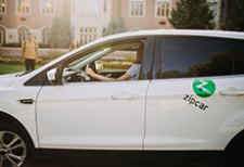 white sedan with Zipcar green dot logo on rear door