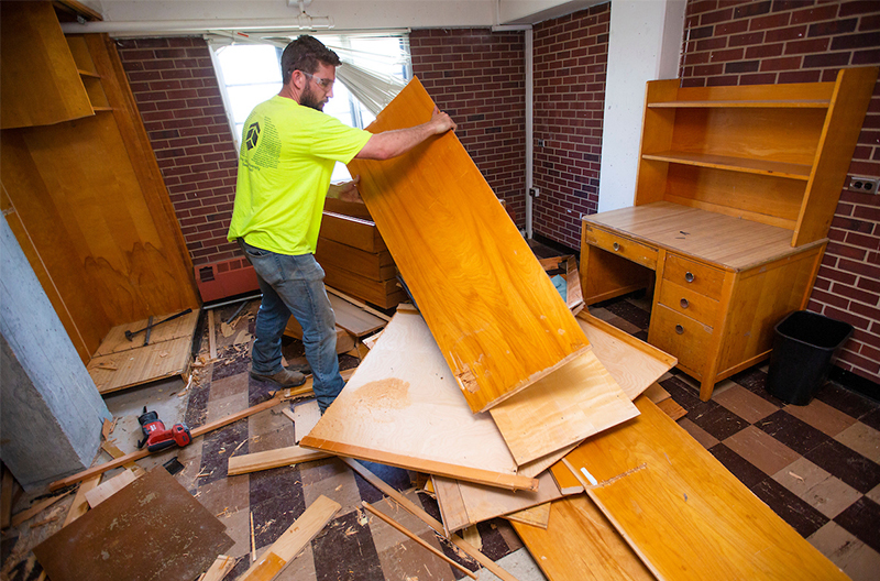 Male worker pulls apart built-in furniture in Helser Hall room