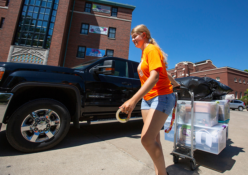 Female student hauls a cart of gear from a car
