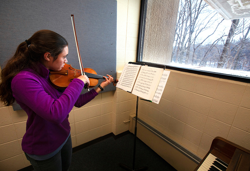 Female student plays violin in small rehearsal room