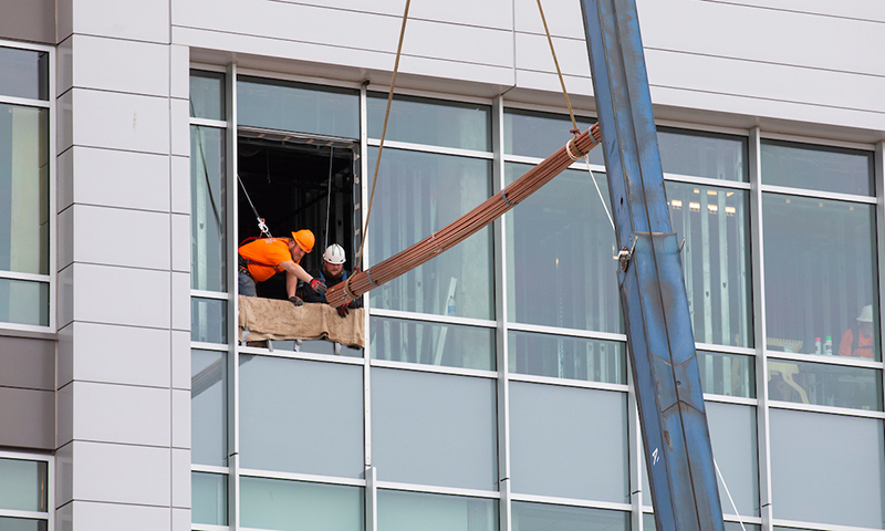 Workers guide copper piping into an open window