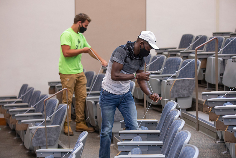 Two male students zip-tie closed theater seats in auditorium