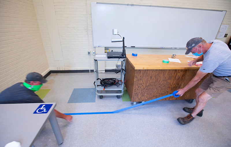 Male employees apply tape to a classroom floor