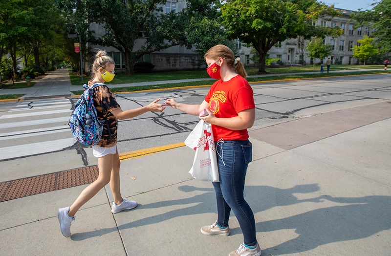 Masked student provides hand sanitizer to another student