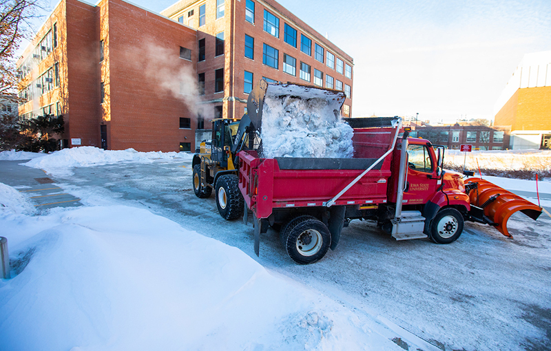 Front loader and dump truck remove snow piles from campus lot