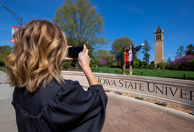Three graduating students take photos at the university wall