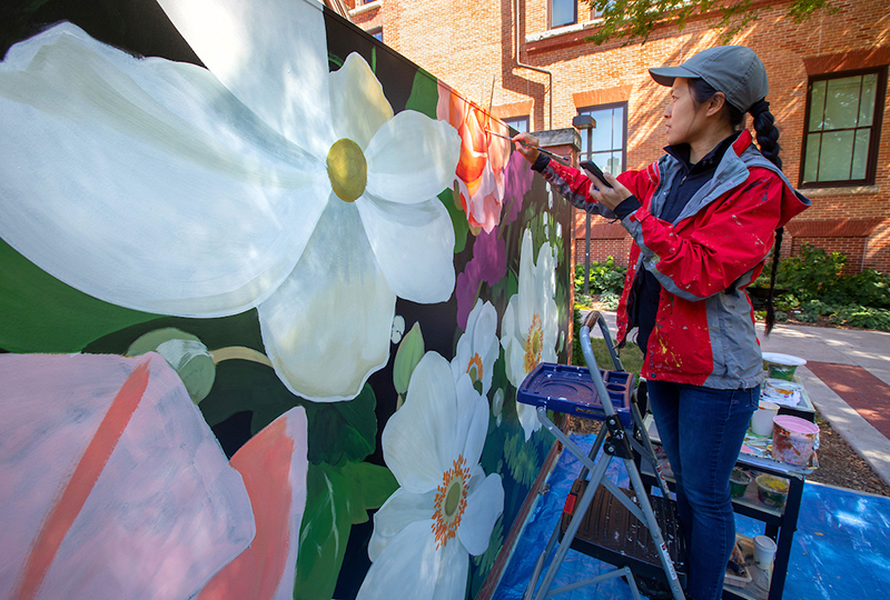 Artist works on large floral mural