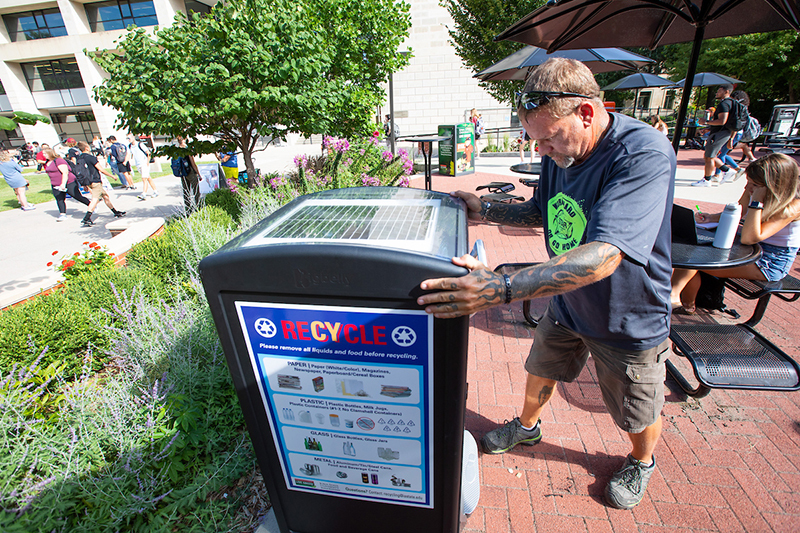 Male employee sets recycling receptacle in place on Hub patio