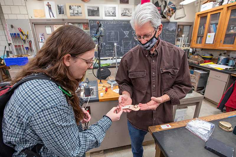 Professor examines brass whistle with student artist