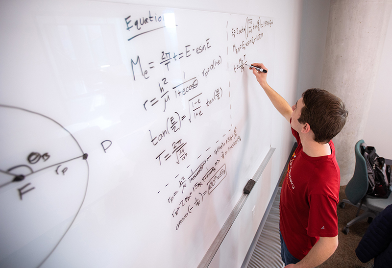 Male student works long equation on whiteboard