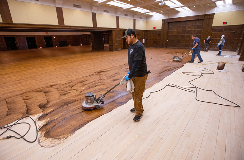 Men apply stain to sanded wood floors