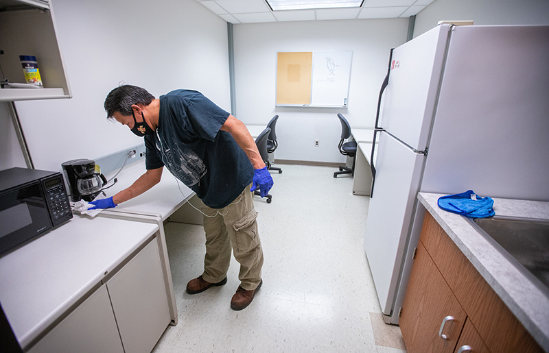 Male custodian cleans table surface in break room