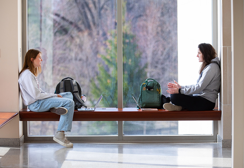 Two female students talk in a window study nook