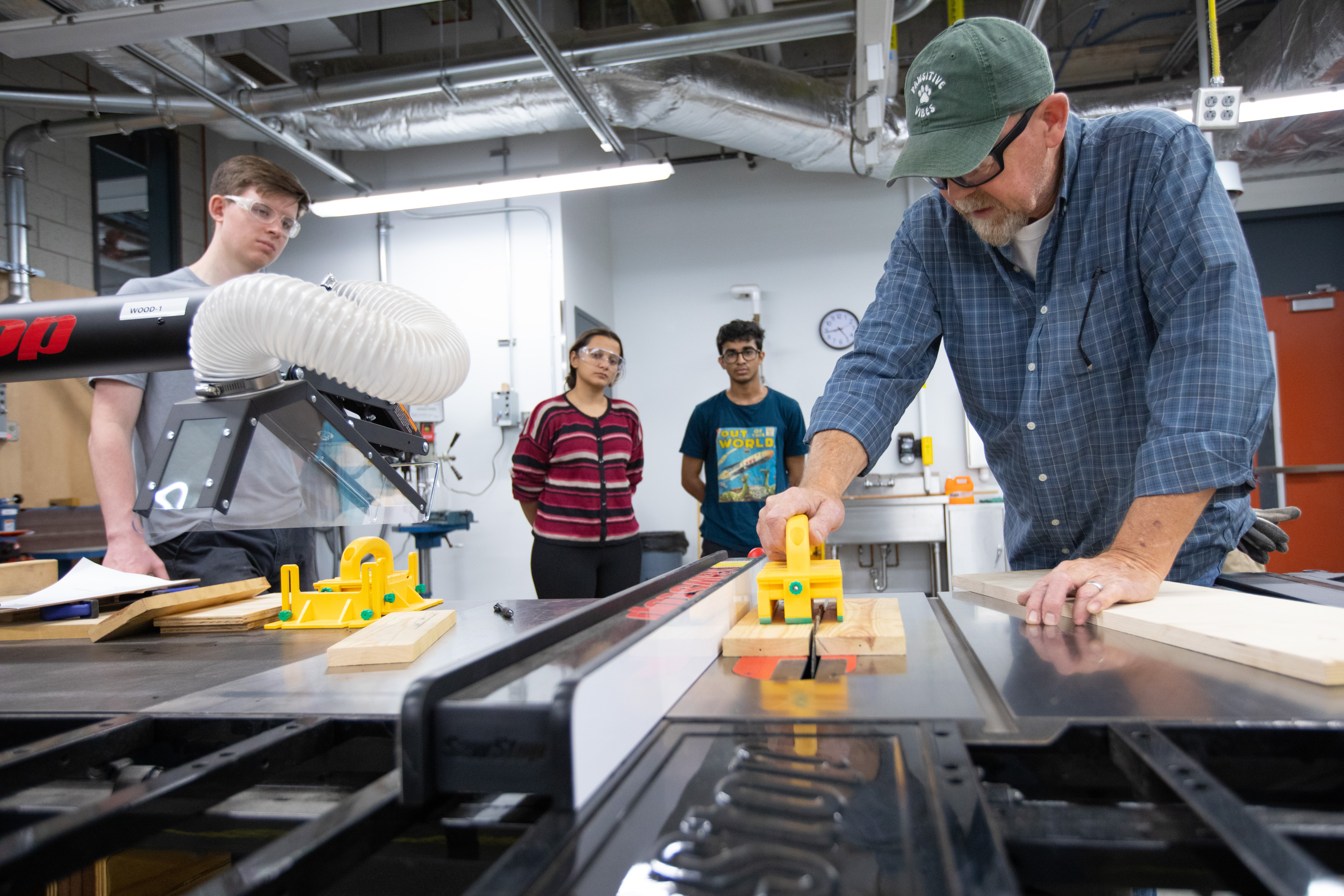 A shop supervisor shows student workers how a table saw works.