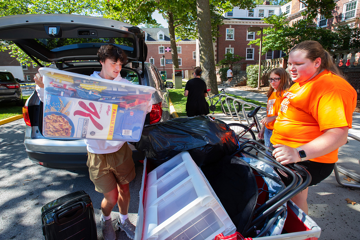 Two student volunteers help male student load red moving cart