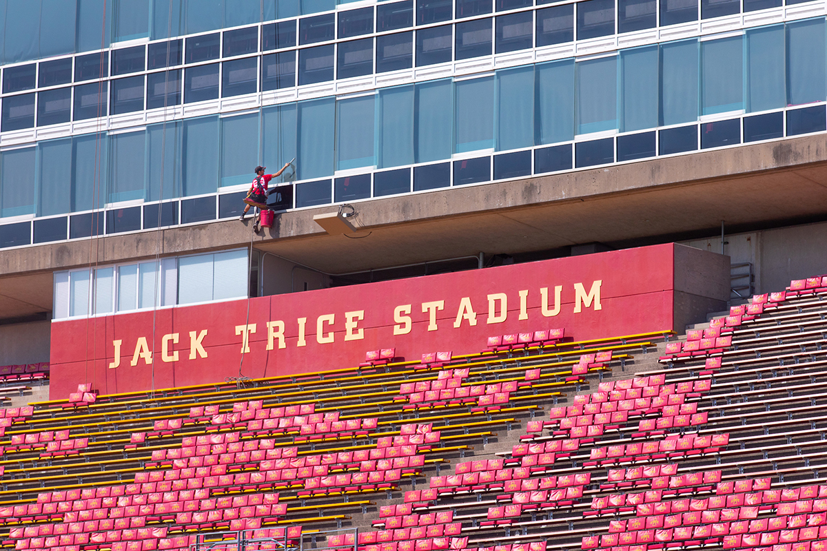 suspended worker cleans press box windows in stadium