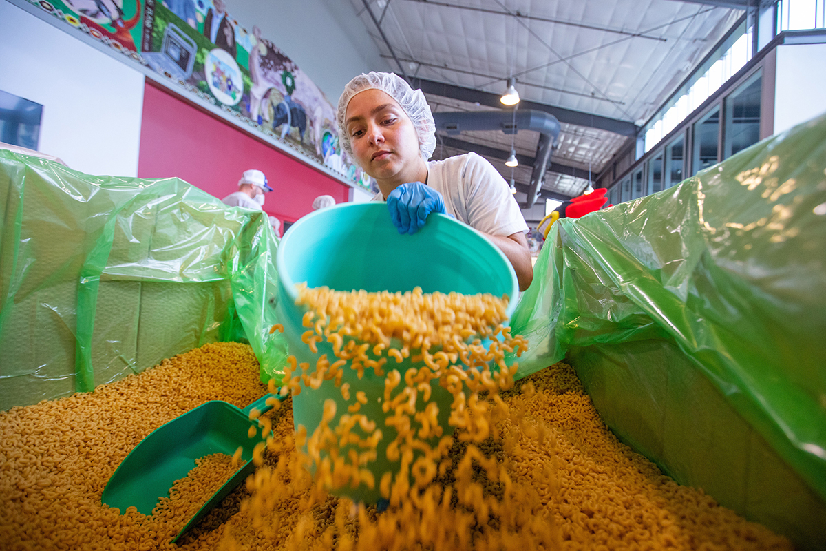 Female student scoops raw macaroni with bucket