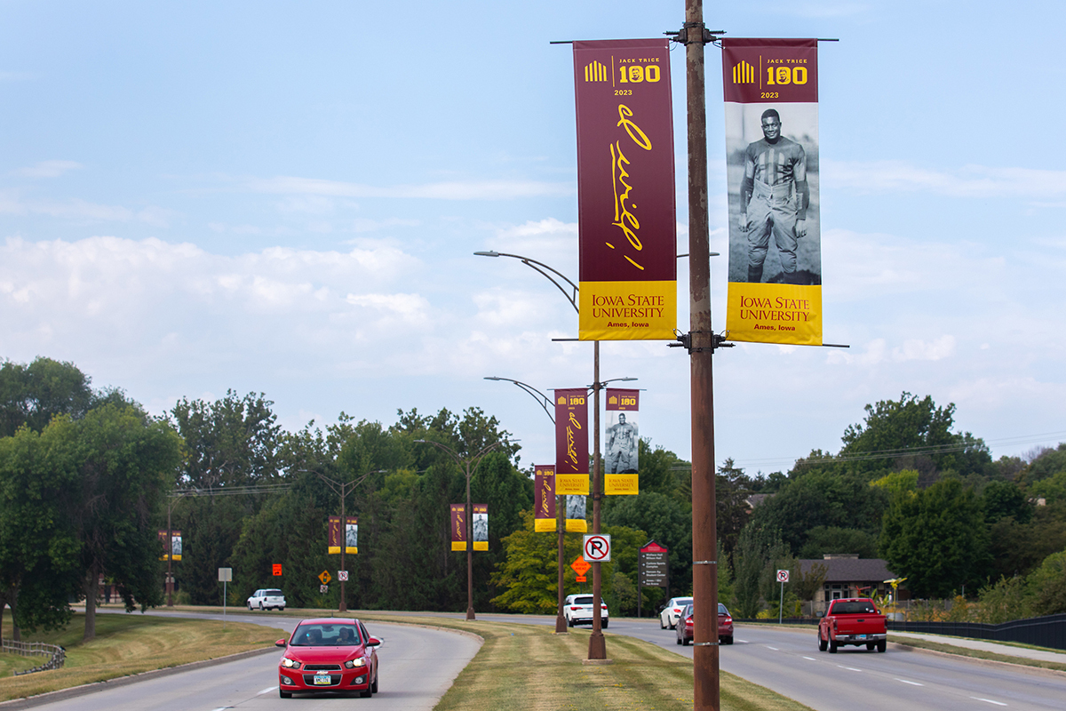 cars drive under Jack Trice lightpole banners on road