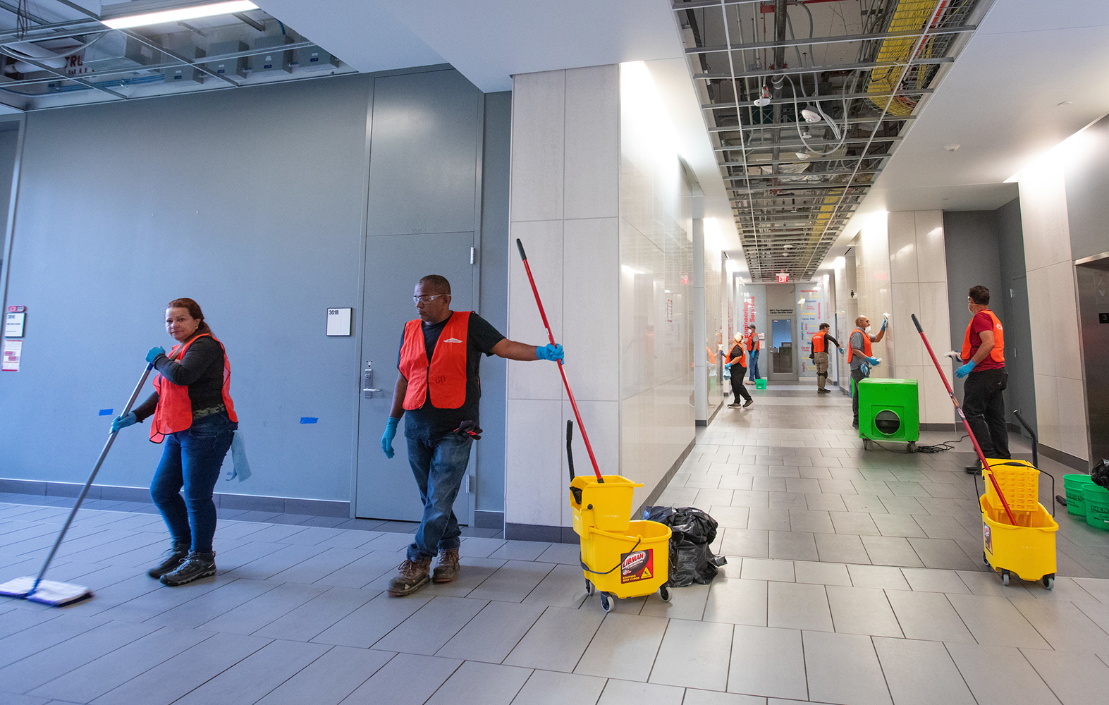 orange-vested workers wash floors and halls