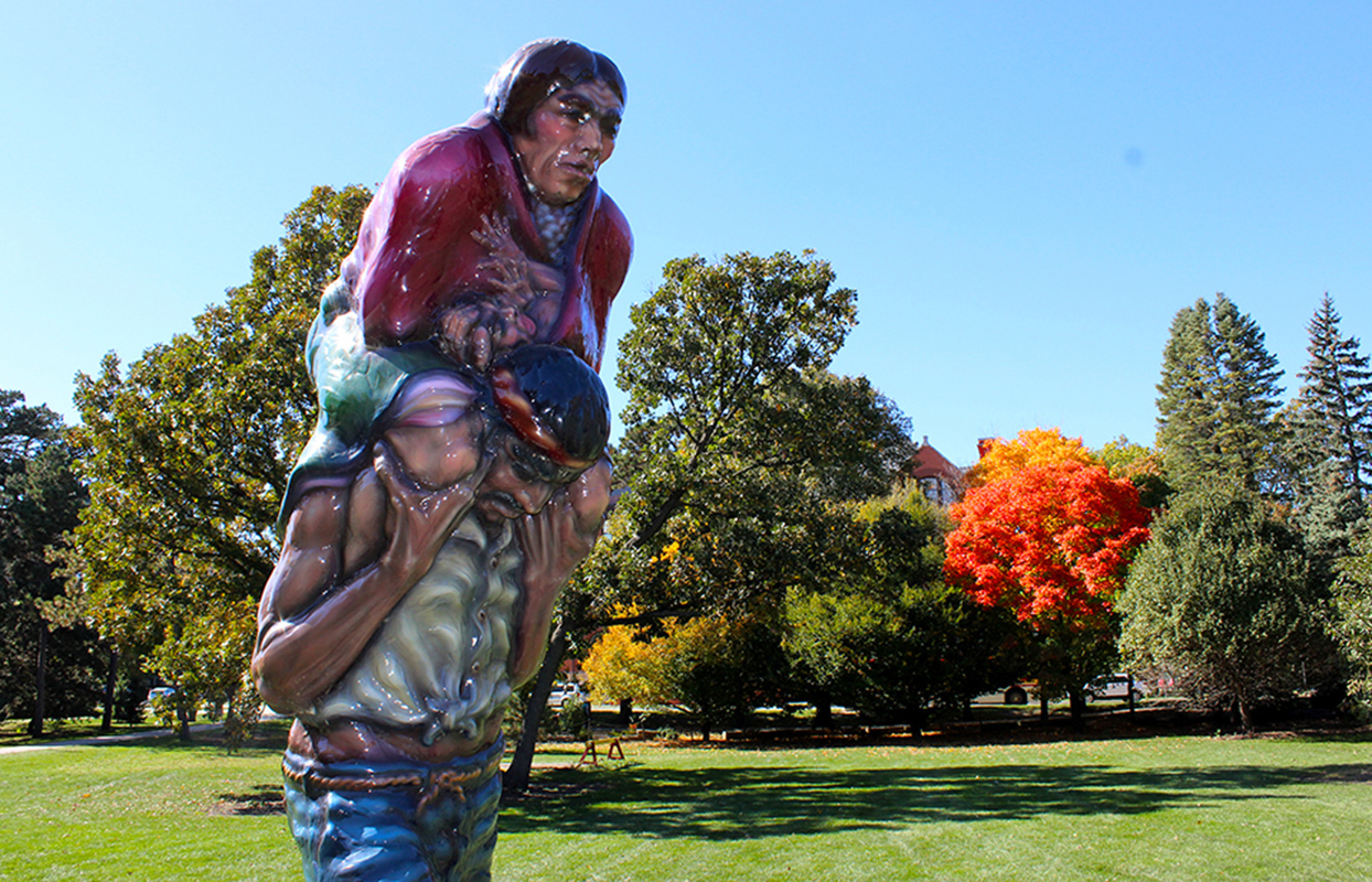 sun reflects off top half of sculpture: man carries woman on his