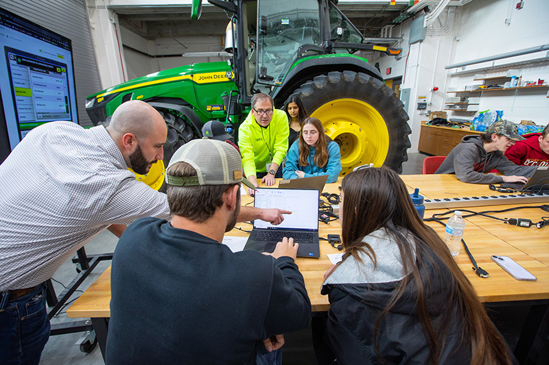 student teams consult laptop data with green tractor behind them