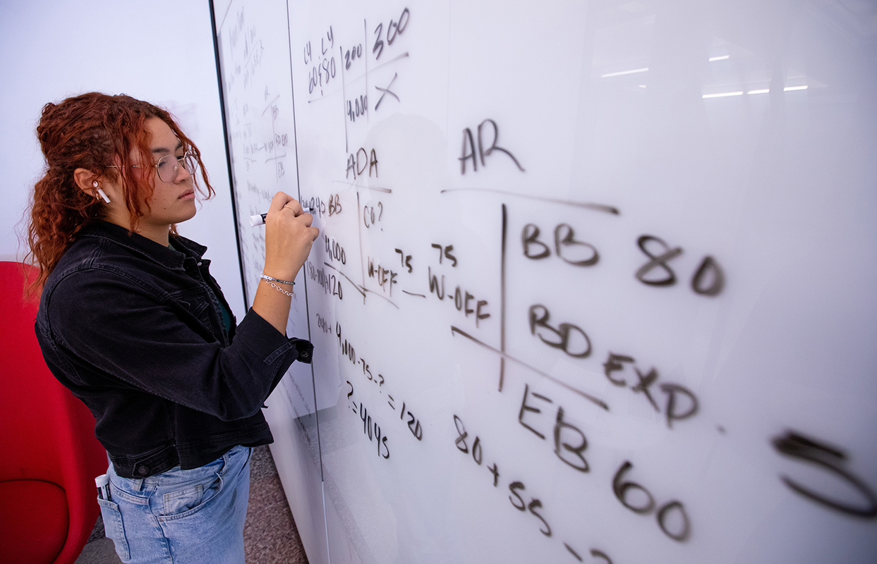 Female Asian student practices answers on a whiteboard