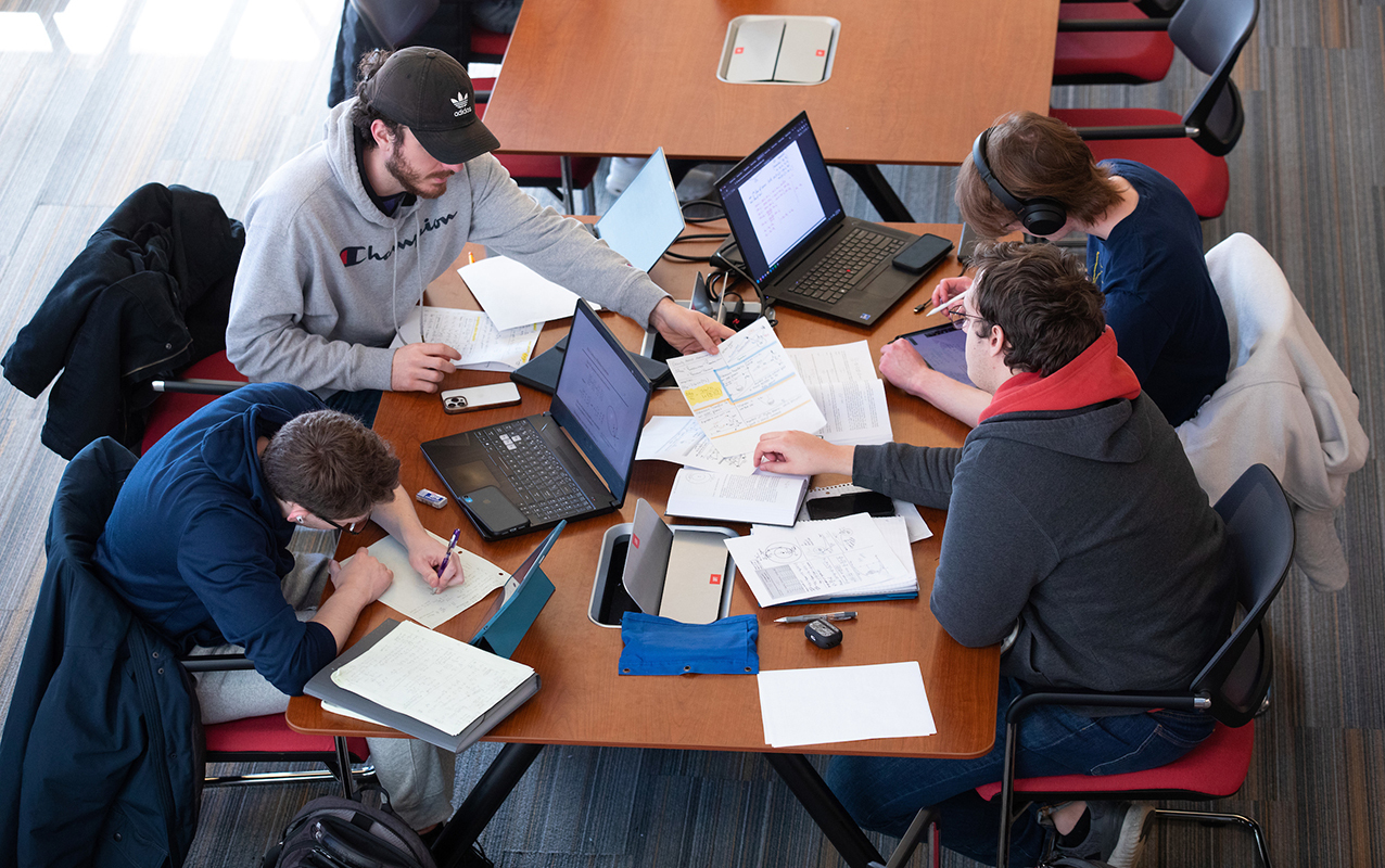 Four male students study together at library table