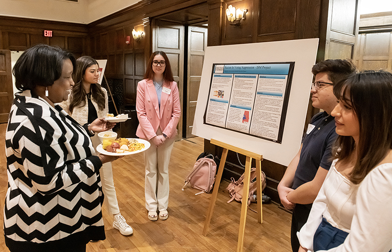 Woman speaks with four female students about a research poster
