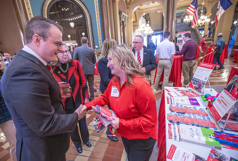 woman in red blouse shakes hands with man in blue suit in capito