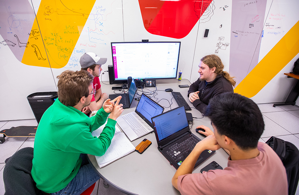 Four male students with laptop computers collaborate at table